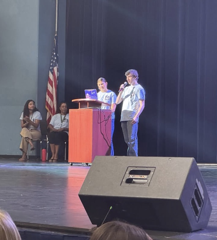 Jonah speaking with a microphone on stage in front of the entire Mira Costa student body